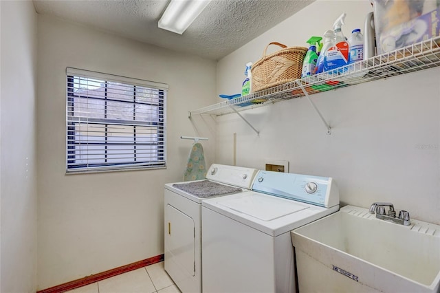 washroom featuring a textured ceiling, light tile patterned floors, sink, and washing machine and clothes dryer