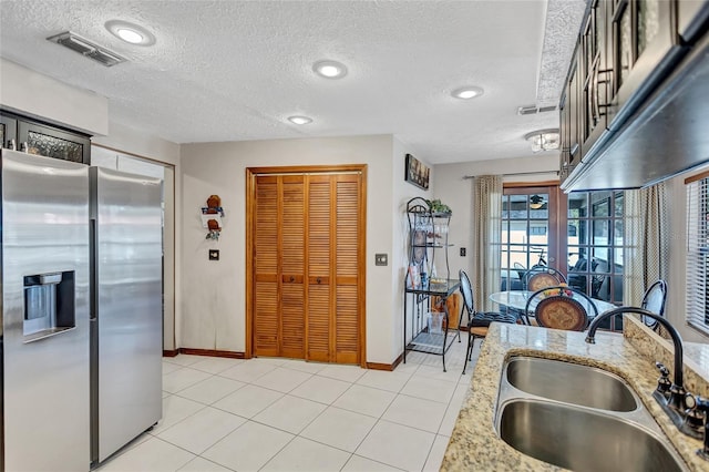 kitchen featuring light tile patterned flooring, stainless steel refrigerator with ice dispenser, a textured ceiling, and sink