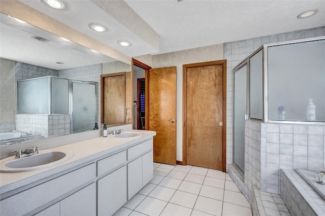 bathroom with a textured ceiling, vanity, plus walk in shower, tile walls, and tile patterned flooring