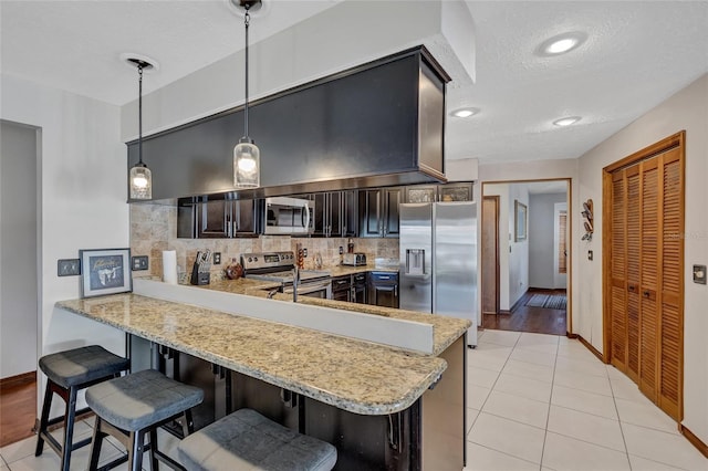 kitchen featuring appliances with stainless steel finishes, tasteful backsplash, decorative light fixtures, light tile patterned flooring, and kitchen peninsula