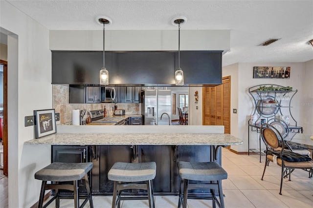 kitchen with kitchen peninsula, appliances with stainless steel finishes, a breakfast bar, and pendant lighting