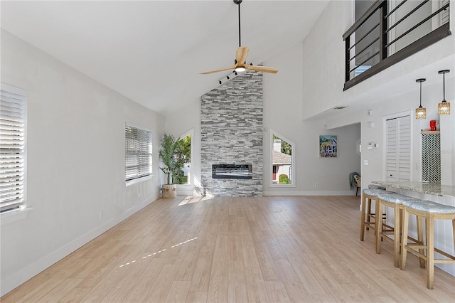 living room with a stone fireplace, ceiling fan, light hardwood / wood-style flooring, and high vaulted ceiling