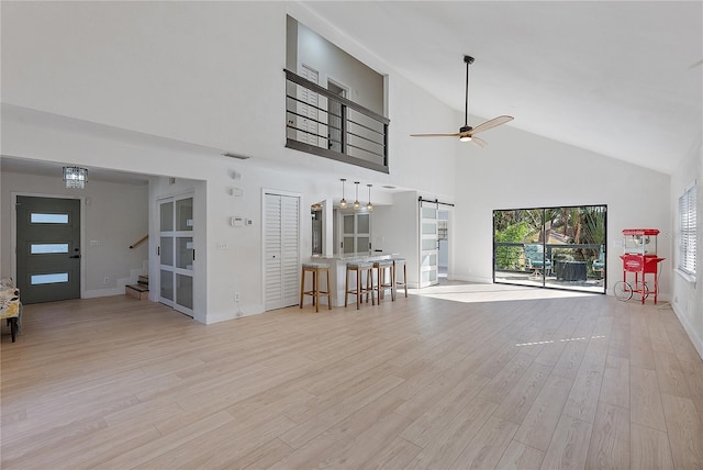 unfurnished living room featuring a barn door, ceiling fan, high vaulted ceiling, and light wood-type flooring