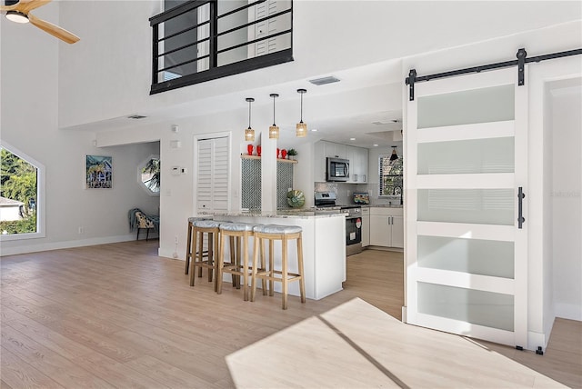 kitchen featuring light wood-type flooring, stainless steel appliances, a barn door, white cabinets, and a breakfast bar area