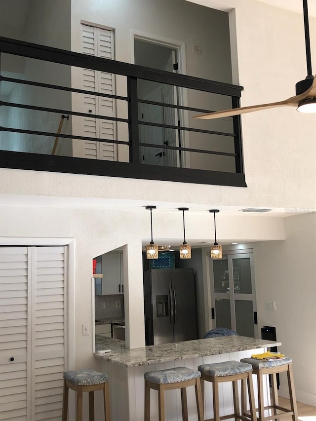 kitchen with light stone countertops, a breakfast bar, decorative light fixtures, and stainless steel refrigerator with ice dispenser