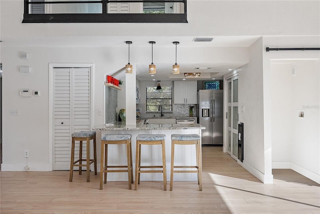 kitchen with a breakfast bar, light stone countertops, light wood-type flooring, appliances with stainless steel finishes, and kitchen peninsula