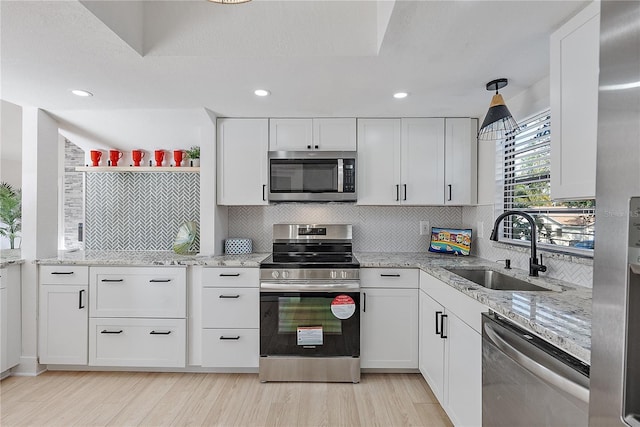 kitchen with white cabinets, sink, light stone countertops, light hardwood / wood-style floors, and stainless steel appliances