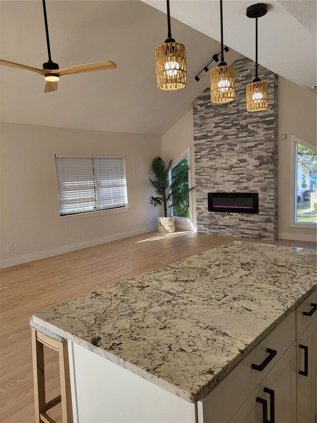 kitchen with a stone fireplace, ceiling fan, light wood-type flooring, decorative light fixtures, and white cabinetry