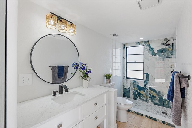 bathroom with hardwood / wood-style flooring, vanity, toilet, and tiled shower