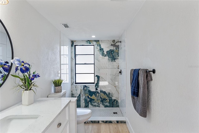 bathroom with hardwood / wood-style flooring, vanity, toilet, and a tile shower