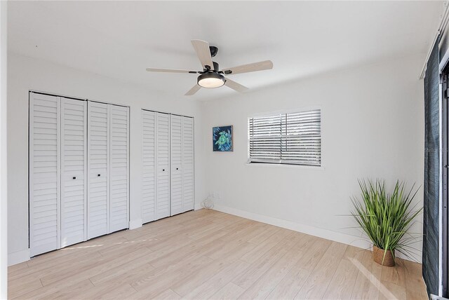 unfurnished bedroom with two closets, light hardwood / wood-style flooring, and ceiling fan