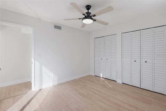 unfurnished bedroom featuring ceiling fan, light hardwood / wood-style floors, and two closets