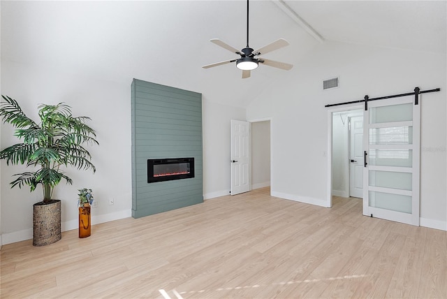 unfurnished living room featuring high vaulted ceiling, light hardwood / wood-style flooring, ceiling fan, a barn door, and beamed ceiling