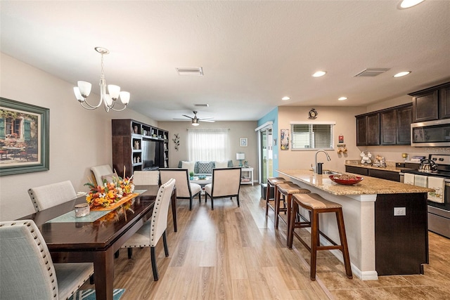 dining space featuring a textured ceiling, ceiling fan with notable chandelier, light wood-type flooring, and sink