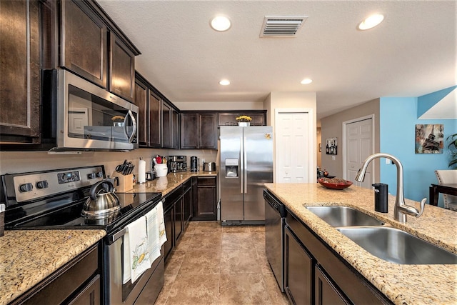 kitchen with sink, light stone countertops, a textured ceiling, appliances with stainless steel finishes, and dark brown cabinetry