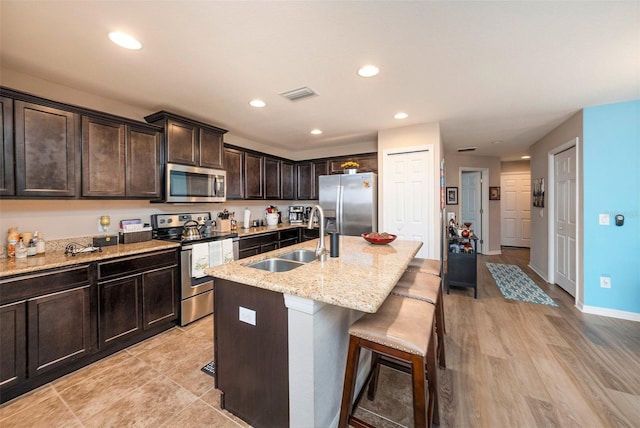 kitchen with appliances with stainless steel finishes, sink, light hardwood / wood-style floors, a breakfast bar area, and an island with sink