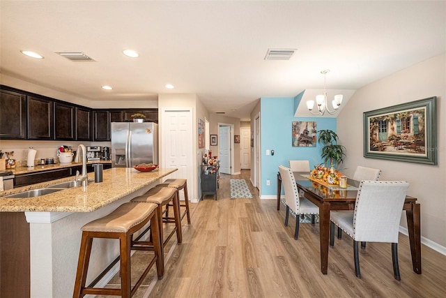 kitchen with stainless steel fridge, light wood-type flooring, light stone counters, sink, and decorative light fixtures