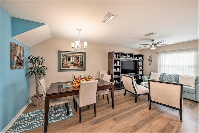 dining space with ceiling fan with notable chandelier, hardwood / wood-style flooring, and lofted ceiling