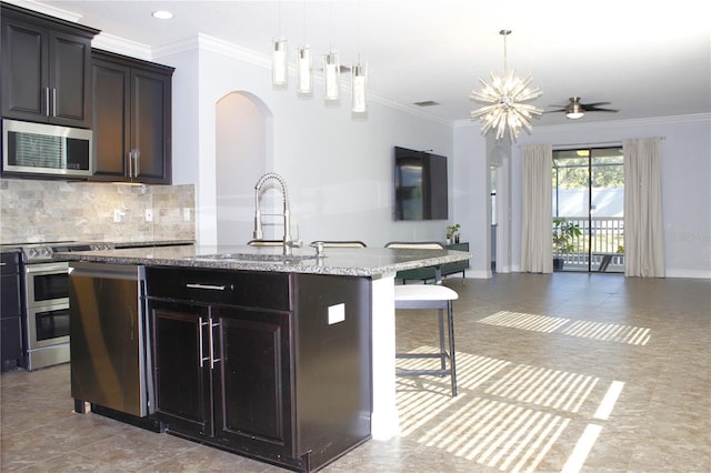 kitchen with sink, hanging light fixtures, ornamental molding, an island with sink, and stainless steel appliances