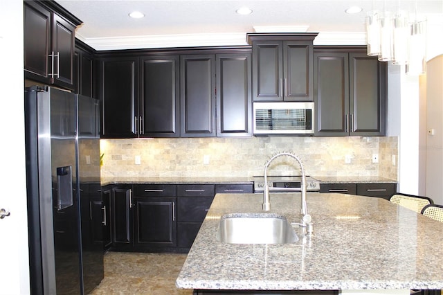 kitchen with light stone countertops, stainless steel appliances, a center island with sink, and sink