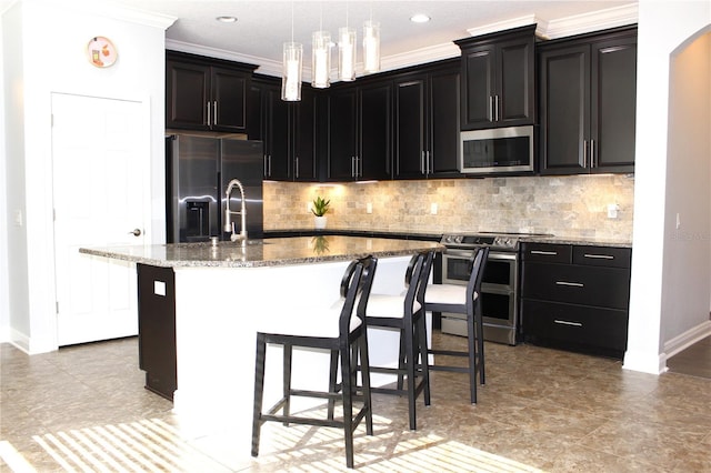 kitchen with stainless steel appliances, light stone counters, an island with sink, pendant lighting, and decorative backsplash