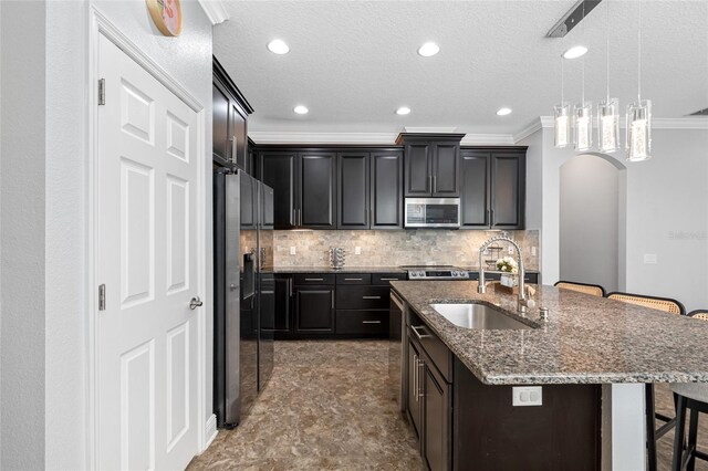 kitchen featuring arched walkways, a kitchen breakfast bar, dark stone countertops, stainless steel appliances, and a sink