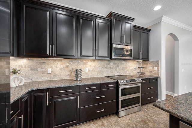 kitchen featuring arched walkways, appliances with stainless steel finishes, ornamental molding, a textured ceiling, and dark cabinetry