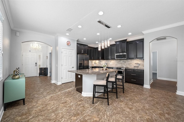 kitchen featuring arched walkways, a kitchen island with sink, appliances with stainless steel finishes, tasteful backsplash, and a kitchen bar