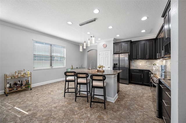 kitchen with tasteful backsplash, arched walkways, appliances with stainless steel finishes, ornamental molding, and a kitchen island with sink