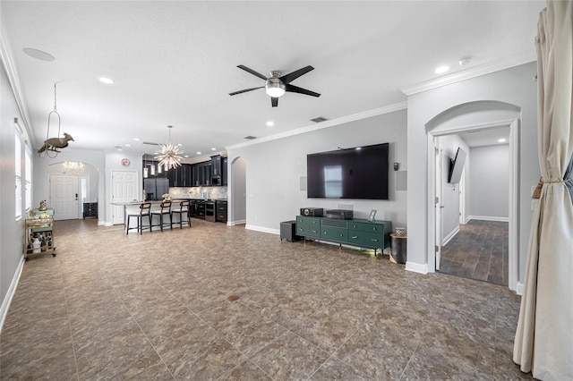 living area with baseboards, arched walkways, ornamental molding, and ceiling fan with notable chandelier