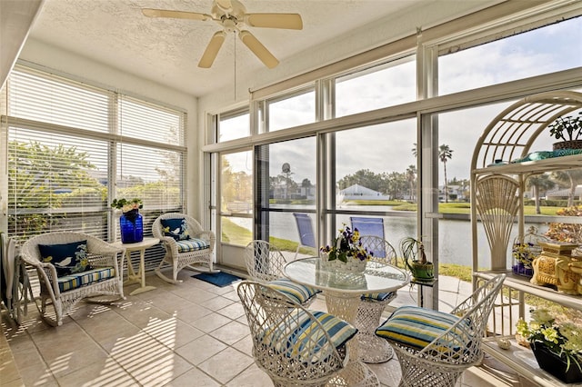 sunroom with ceiling fan and a water view