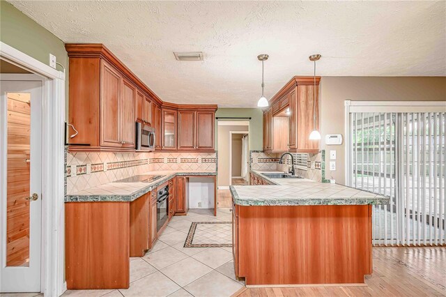 kitchen with oven, light wood-type flooring, tasteful backsplash, decorative light fixtures, and kitchen peninsula