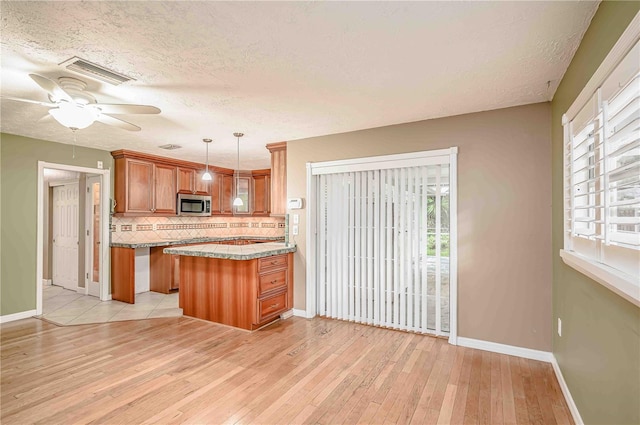 kitchen featuring kitchen peninsula, tasteful backsplash, a textured ceiling, pendant lighting, and light hardwood / wood-style flooring