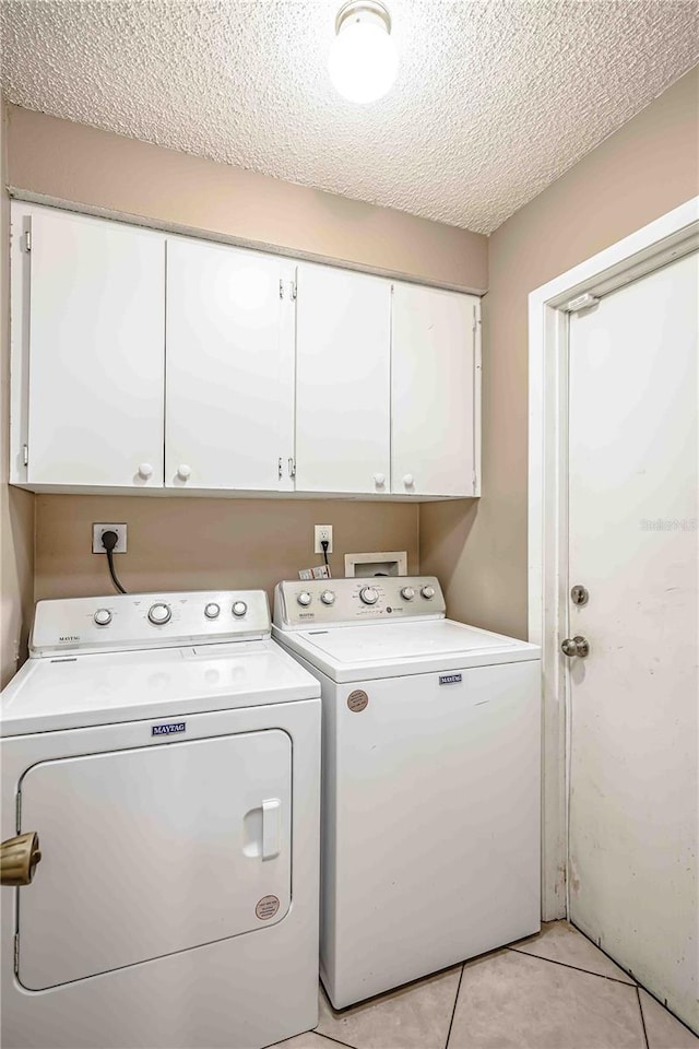 clothes washing area featuring cabinets, light tile patterned floors, a textured ceiling, and washer and clothes dryer