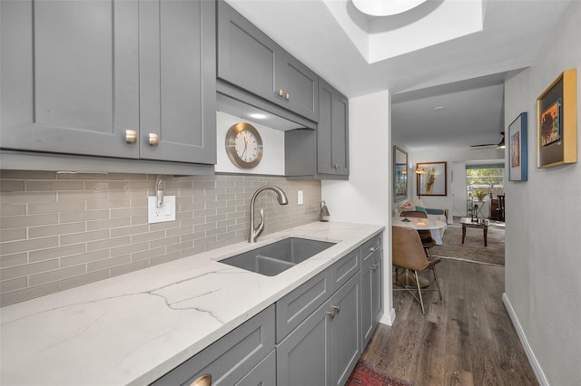 kitchen with gray cabinetry, sink, dark hardwood / wood-style floors, decorative backsplash, and light stone counters