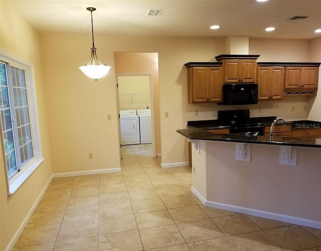 kitchen with pendant lighting, dark stone counters, black appliances, washing machine and dryer, and light tile patterned floors