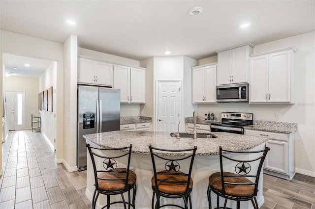 kitchen featuring white cabinets, a center island with sink, sink, light stone countertops, and appliances with stainless steel finishes