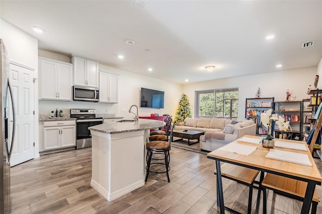 kitchen with white cabinets, stainless steel appliances, light stone countertops, and a center island with sink