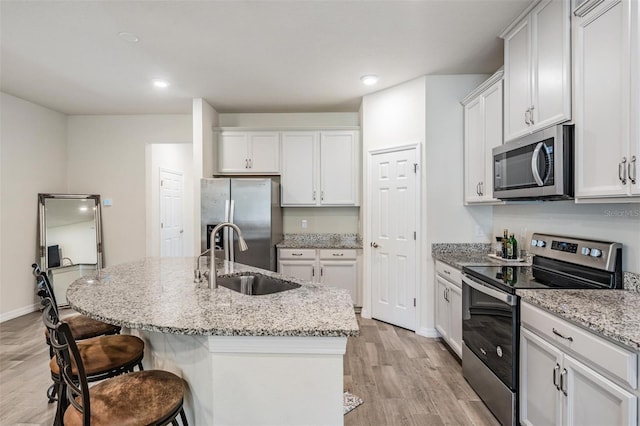 kitchen with light stone countertops, sink, stainless steel appliances, light hardwood / wood-style flooring, and an island with sink