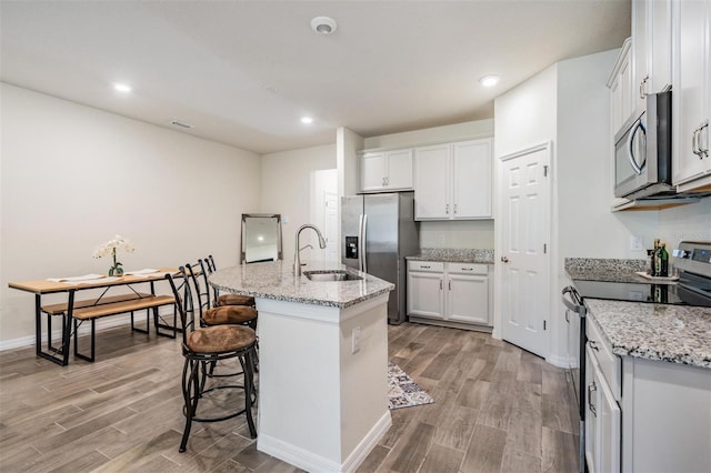 kitchen with a center island with sink, sink, light stone countertops, appliances with stainless steel finishes, and white cabinetry