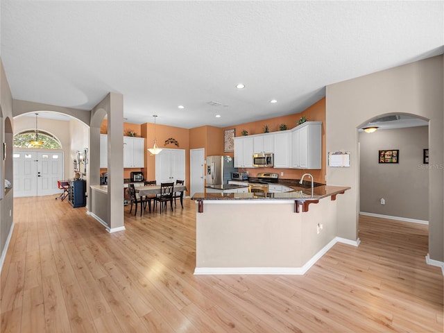 kitchen featuring white cabinets, light hardwood / wood-style floors, kitchen peninsula, pendant lighting, and appliances with stainless steel finishes