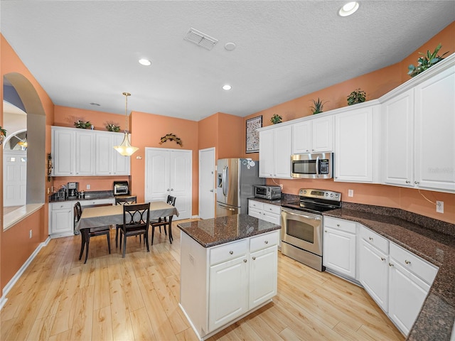 kitchen featuring decorative light fixtures, appliances with stainless steel finishes, light hardwood / wood-style floors, and white cabinetry