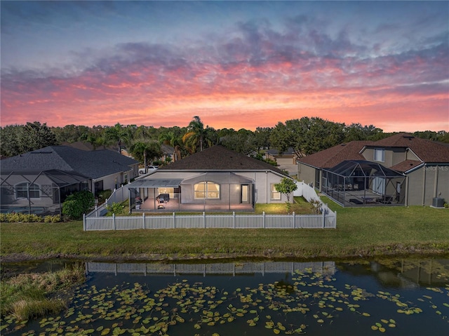 back house at dusk with a yard, a water view, and glass enclosure