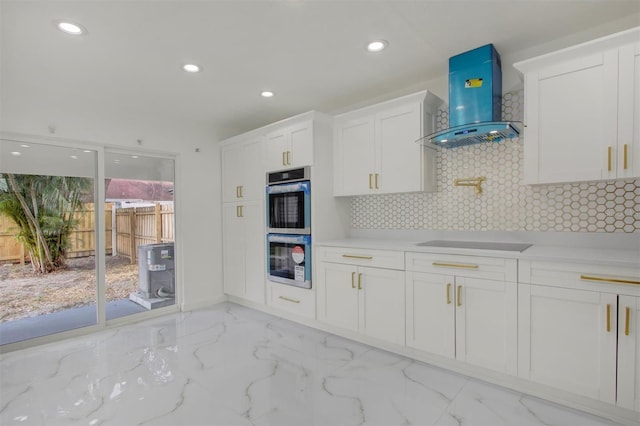 kitchen featuring white cabinetry, stovetop, stainless steel double oven, and wall chimney range hood