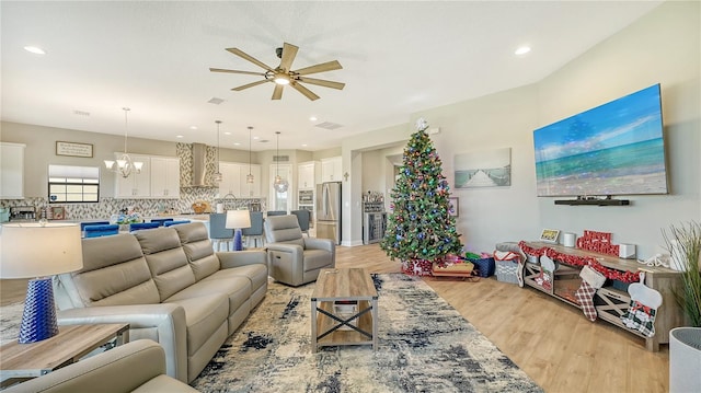 living room with ceiling fan with notable chandelier and light hardwood / wood-style floors