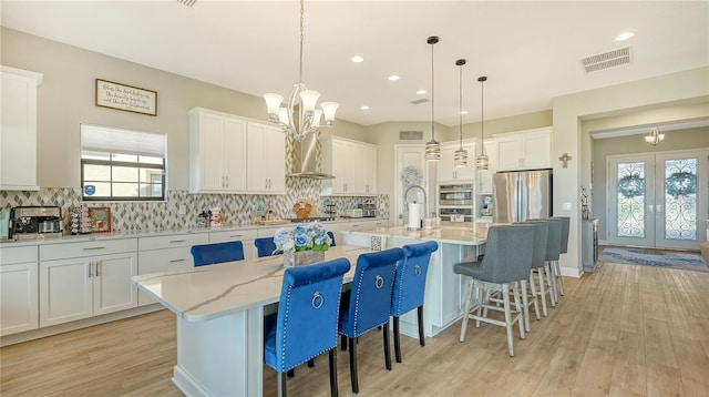 kitchen with white cabinets, decorative light fixtures, stainless steel appliances, and an island with sink