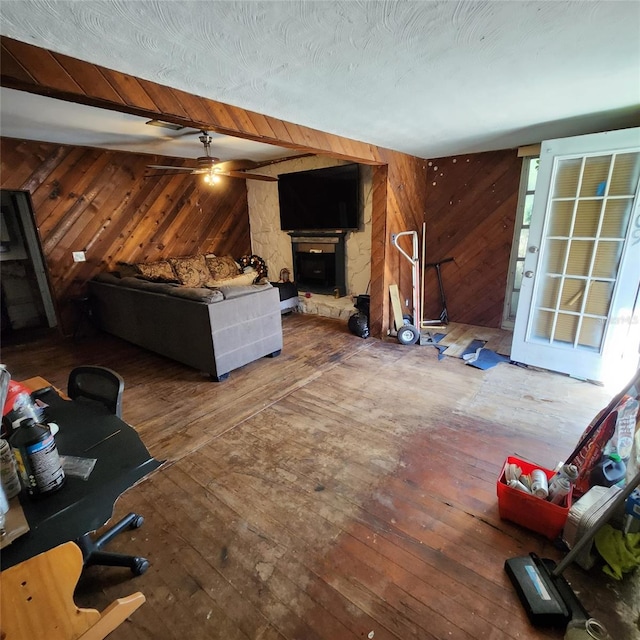 living room featuring beam ceiling, ceiling fan, wood walls, wood-type flooring, and a fireplace