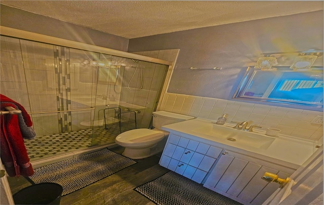 bathroom with a textured ceiling, vanity, tile walls, toilet, and a shower with shower door