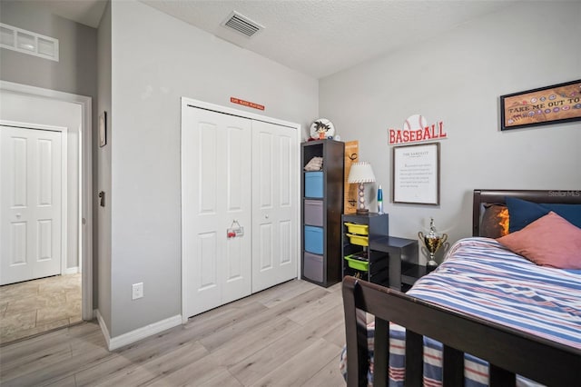 bedroom with light hardwood / wood-style floors, a textured ceiling, and a closet