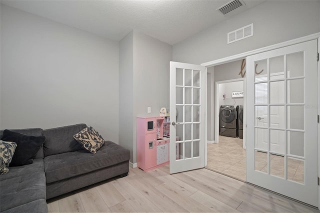 living room featuring washer and dryer, french doors, light wood-type flooring, and a textured ceiling